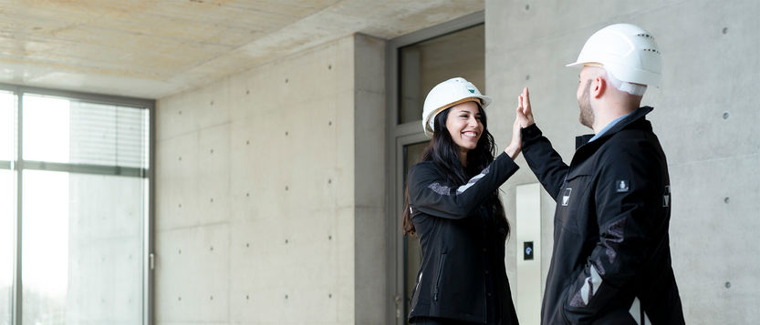 A woman and a man with construction helmet and weisenburger jacket slap a high five