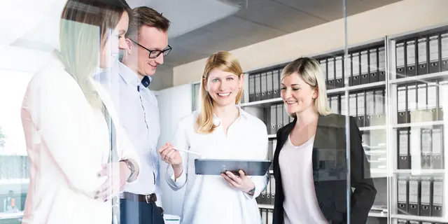 weisenburger-Projektentwicklung-Team Mitarbeiter sehen sich etwas auf Tablet an, hinter ihnen ein Schrank voller Ordner