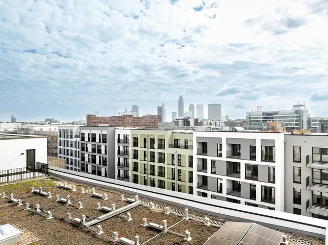 weisenburger-Gruppe: Wohnanlage in Frankfurt Wohngebäude in einem Neubaugebiet mit Blick auf die Skyline von Frankfurt am Main bei bewölktem Himmel.