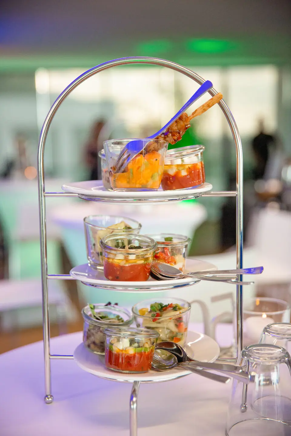 Etagere with culinary highlights for weisenburg anniversary event Three-tier metal etagere with several small glasses presenting various culinary appetizers