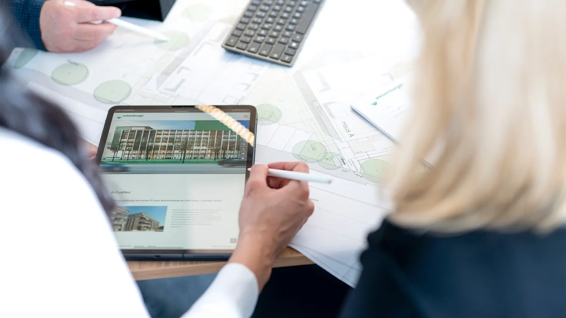 Innovation Header Tablet Mehrere Personen beugen sich über einen Bauplan und ein Tablet