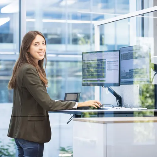 Die Abteilung Kalkulation bei weisenburger Eine junge Frau steht an einem höhenverstellbaren Schreibtisch und lächelt