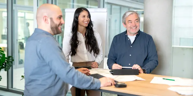 Über uns Meeting Zwei Maenner und eine Frau besprechen sich an einem Stehtisch