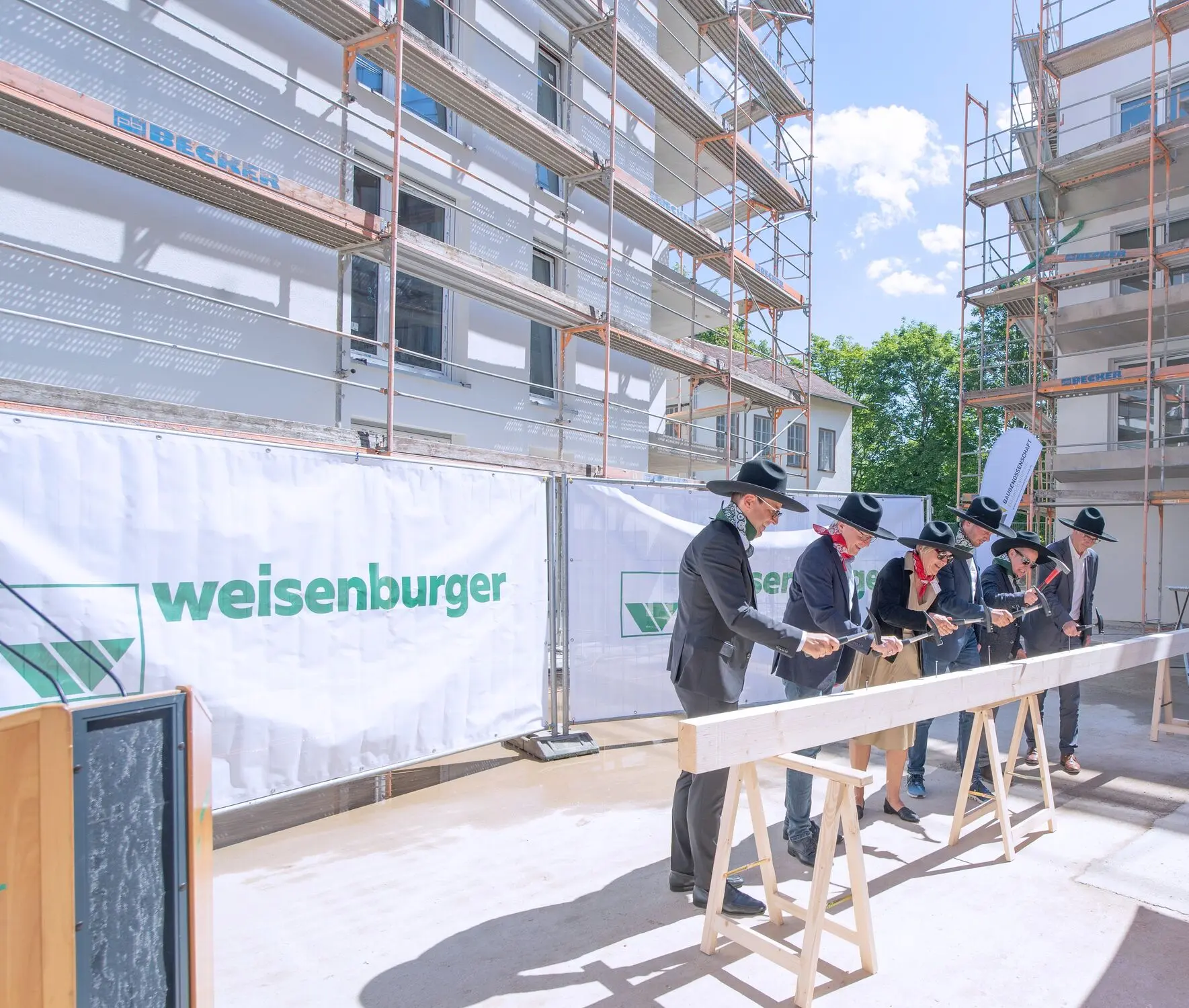 Topping-out ceremony in Baden-Baden 2024 weisenburger bau celebrates construction progress Five men and one woman hammer nails into a wooden beam at the topping-out ceremony for weisenburger bau in Baden-Baden