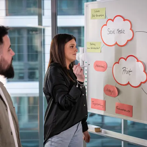 Die Marketing-Abteilung bei weisenburger Ein junger Mann und eine junge Frau stehen vor einem Whiteboard und sind auf der Ideensuche