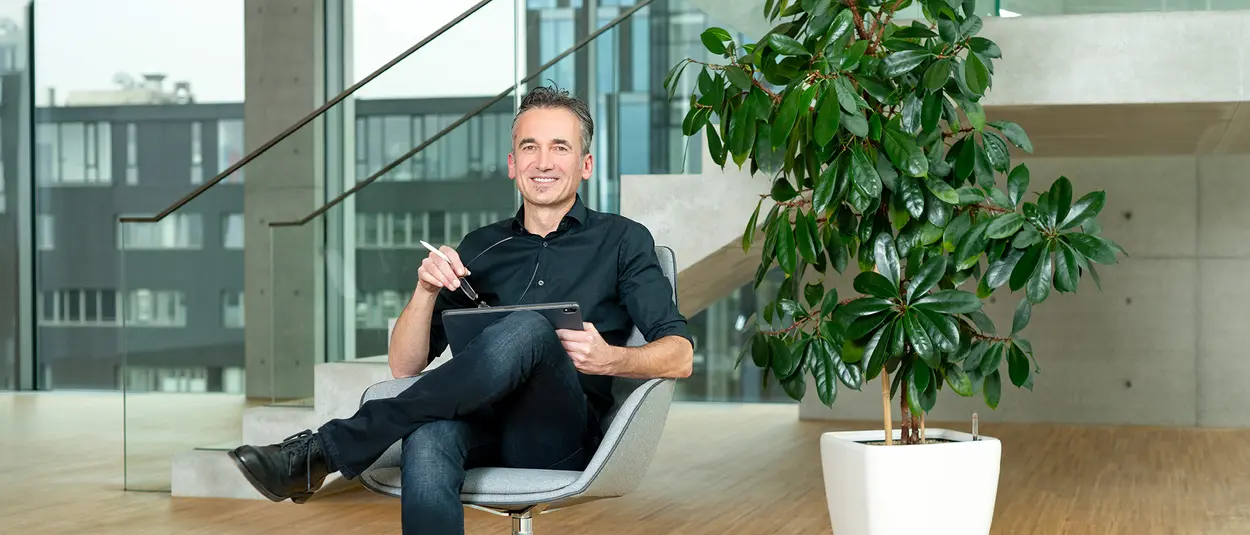 Processing and support A man sits cross-legged in a chair and looks at the camera smiling
