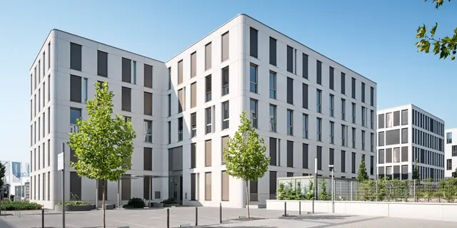 Gewerbebau-weisenburger-bau Außenansicht weisenburger Gewerbebau in weiß mit Fenstern, Stellplätzen und blauem Himmel