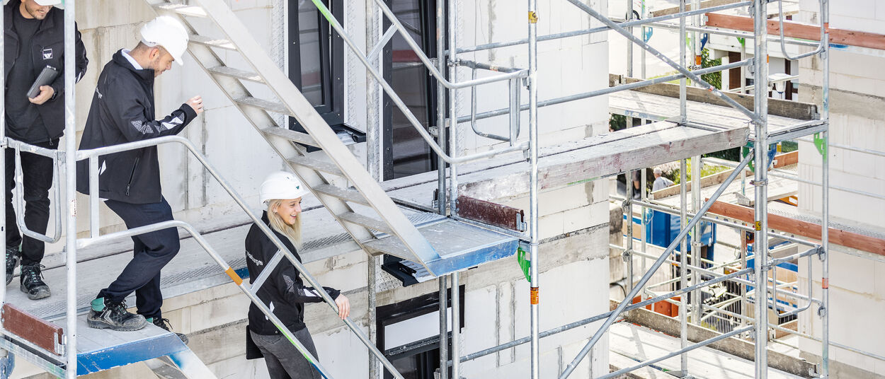 zwei Männer und eine Frau besichtigen eine weisenburger Baustelle und laufen dabei ein Gerüst herunter