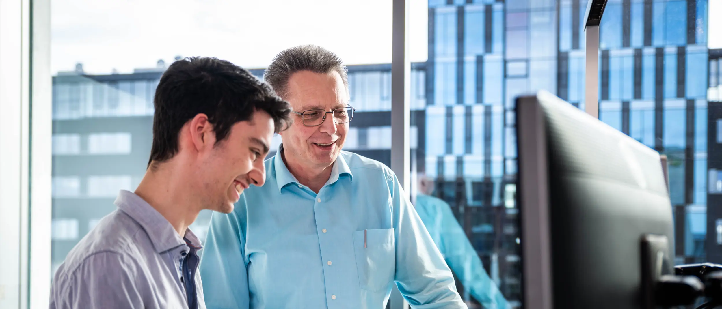 Ausbildung bei weisenburger als Fachinformatiker Zwei Männer stehen in einem Büro und schauen auf einen Bildschirm