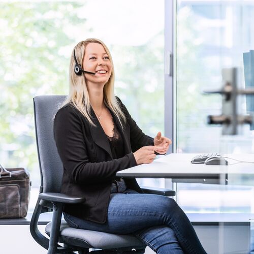 eine junge Frau sitzt an einem Schreibtisch und telefoniert mit einem Headset auf ihrem Kopf