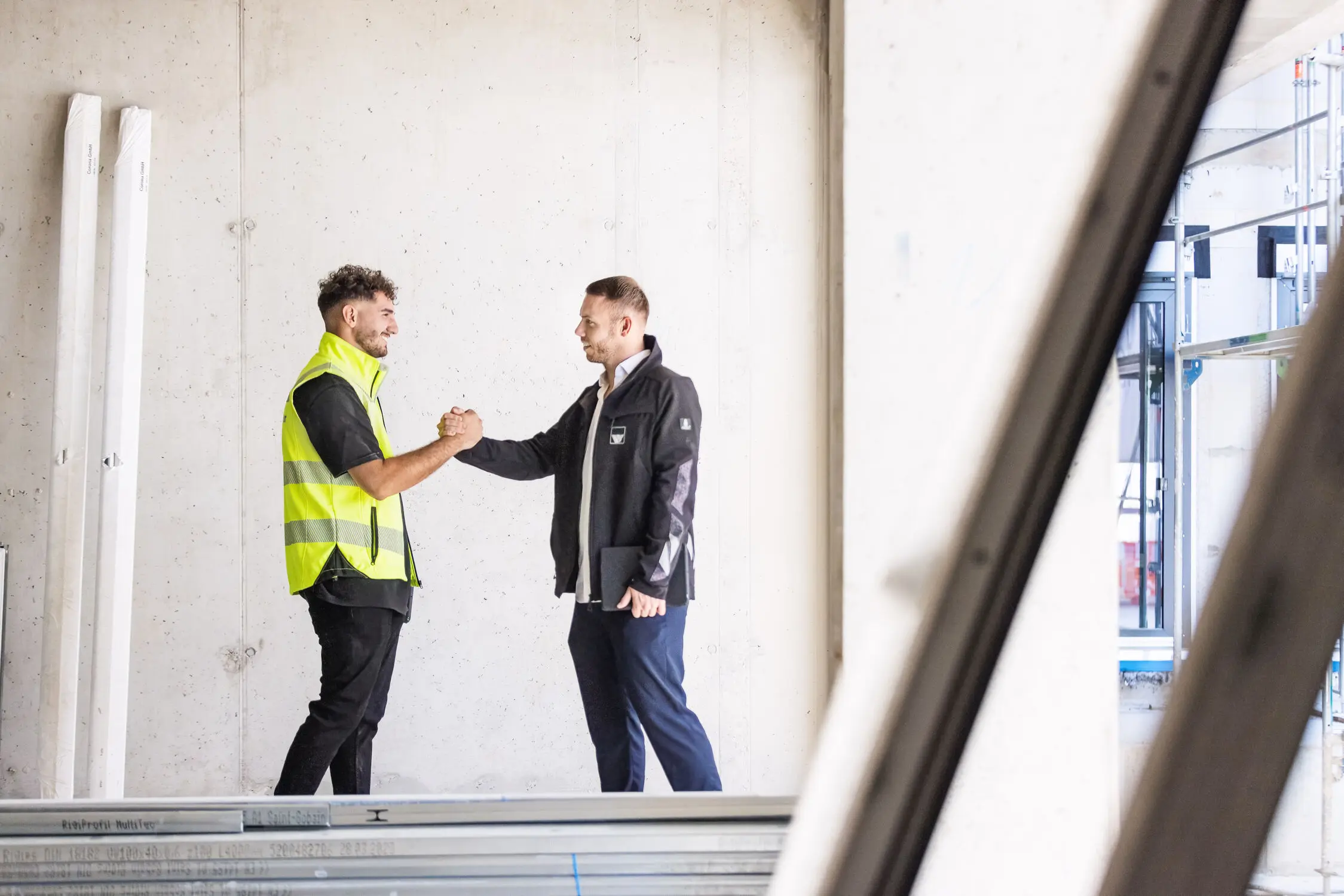 Ein Berufseinsteiger und der Ausbilder sind auf einer weisenburger Baustelle Zwei Männer mit weisenburger Jacken begrüßen sich gegenseitig mit einem Handschlag