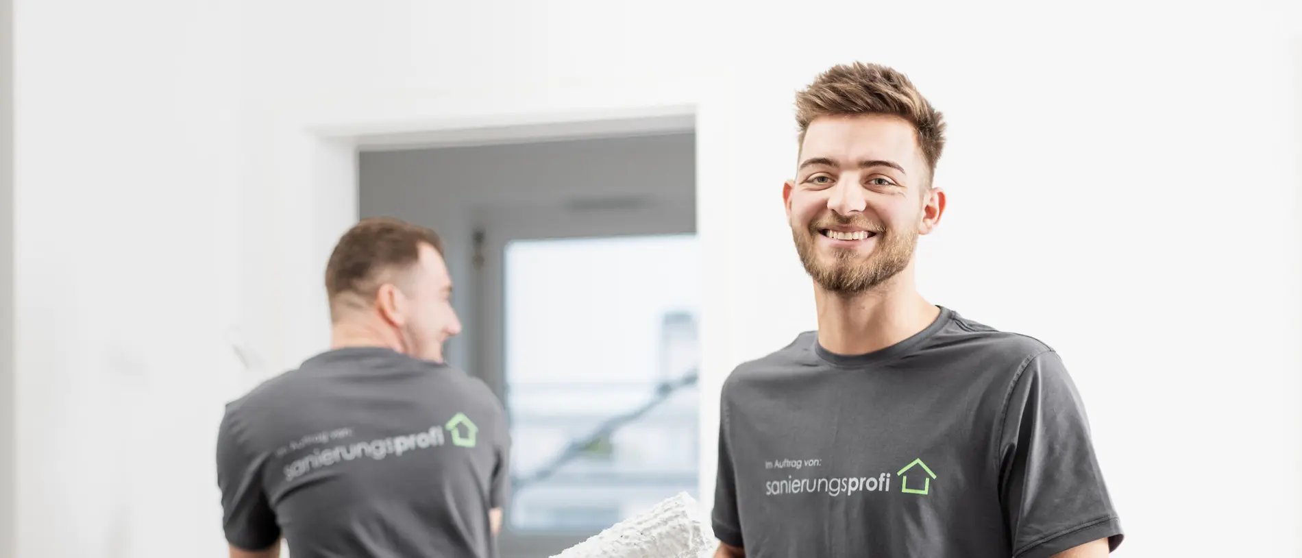 sanierungsprofi Malerarbeiten bei Gebäudesanierung Zwei Mitarbeiter von sanierungsprofi streichen mit weißer Farbe die Innenräume eines Gebäudes