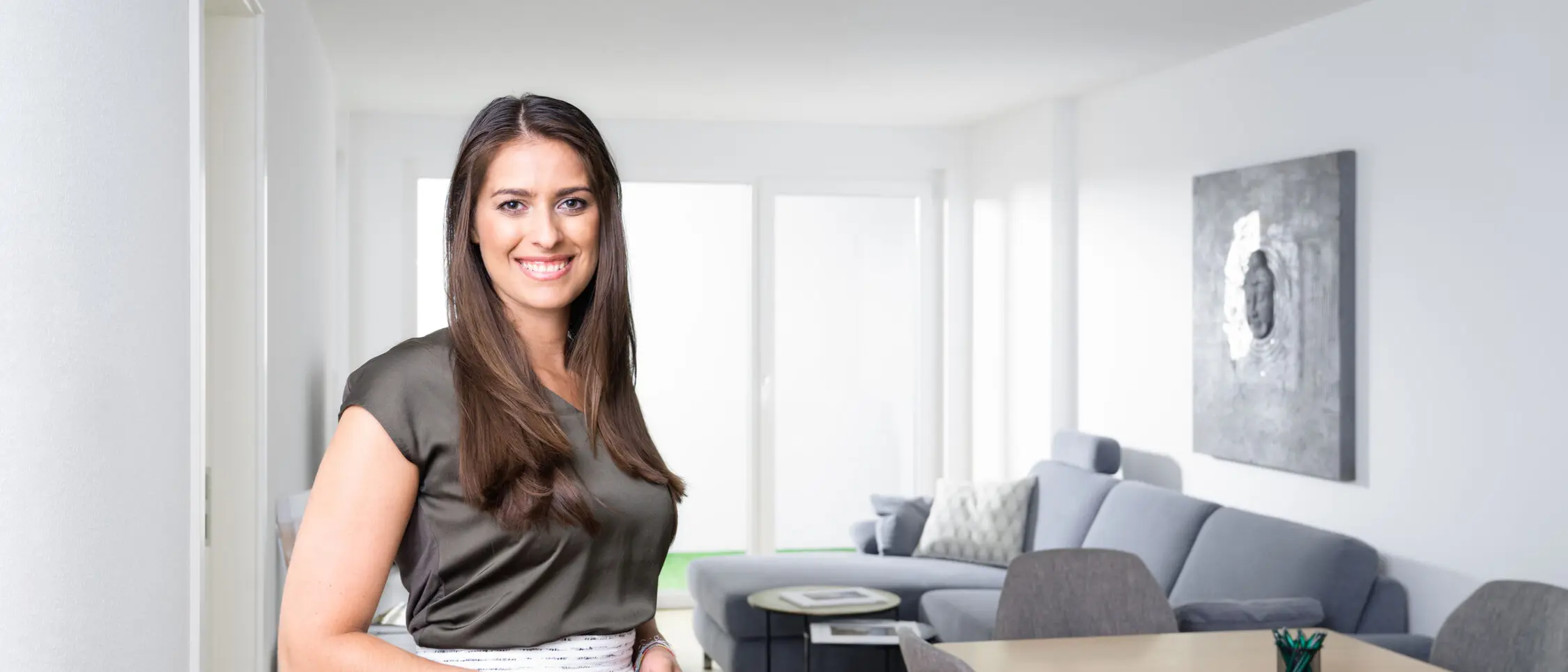 weisenburger Bemusterungszentrum baustein Eine Frau steht in einem Wohn-und Essbereich im weisenburger-Musterhaus und lächelt in die Kamera