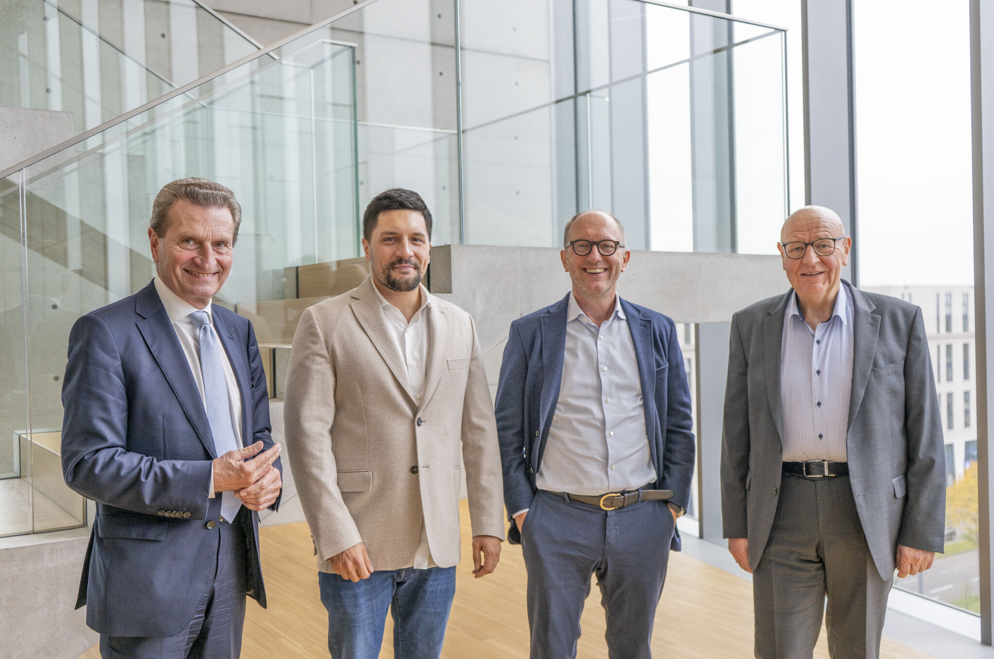 vier Männer in Businesskleidung nebeneinander in einem modernen Gebäude mit Glas- und Beton-Elementen