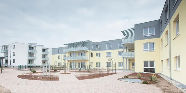 Pflegeeinrichtung-Iffezheim-Außenanlage Innenhof der von weisenburger erbauten Pflegeeinrichtung in Iffezheim mit gelber Hausferssade