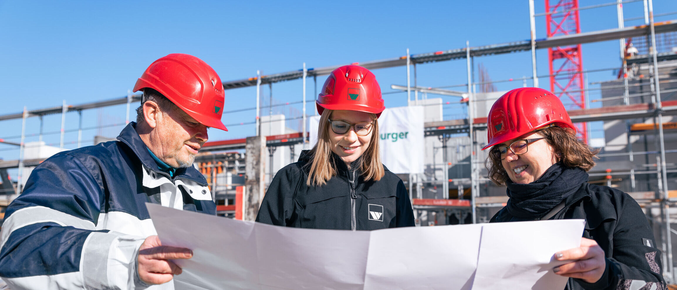 drei Bauleiter der Firma weisenburger stehen auf einer Baustelle und studieren einen Bauplan 