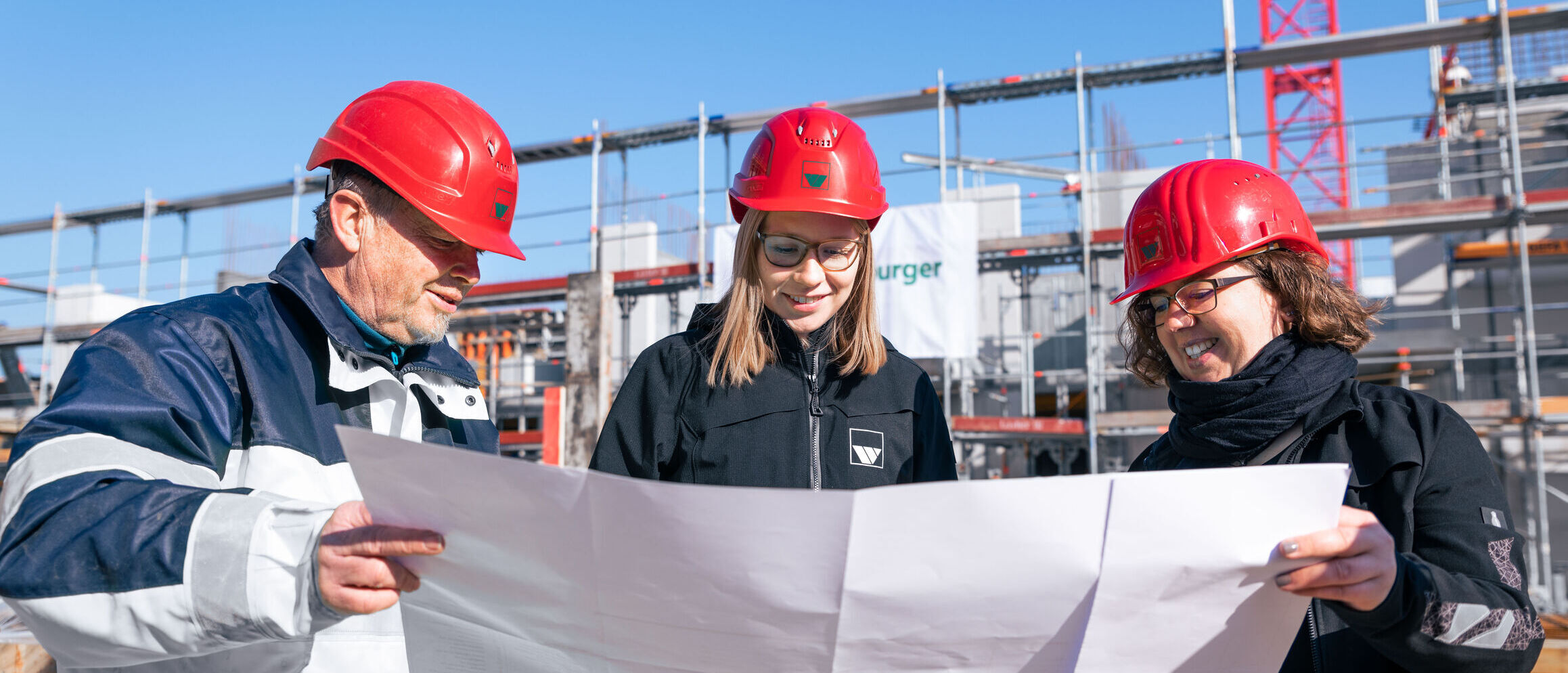 drei Bauleiter der Firma weisenburger stehen auf einer Baustelle und studieren einen Bauplan 