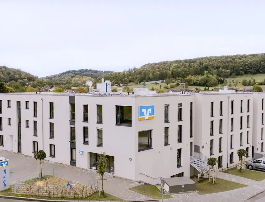 Gewerbebau mit Volksbank Filiale und Parkplatz Moderne Gewerbeeinrichtung mit Volksbank Filiale, gepflasterten Parkplätzen und Spielplatz bei blauem Himmel