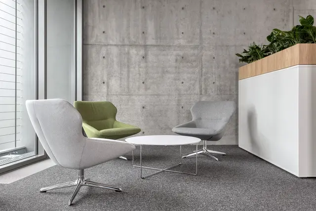 Sitzmöglichkeit © Nikolay Kazakov Drei bequeme Stühle stehen um einen niedrigen weißen Tisch vor einer Sichtbetonwand