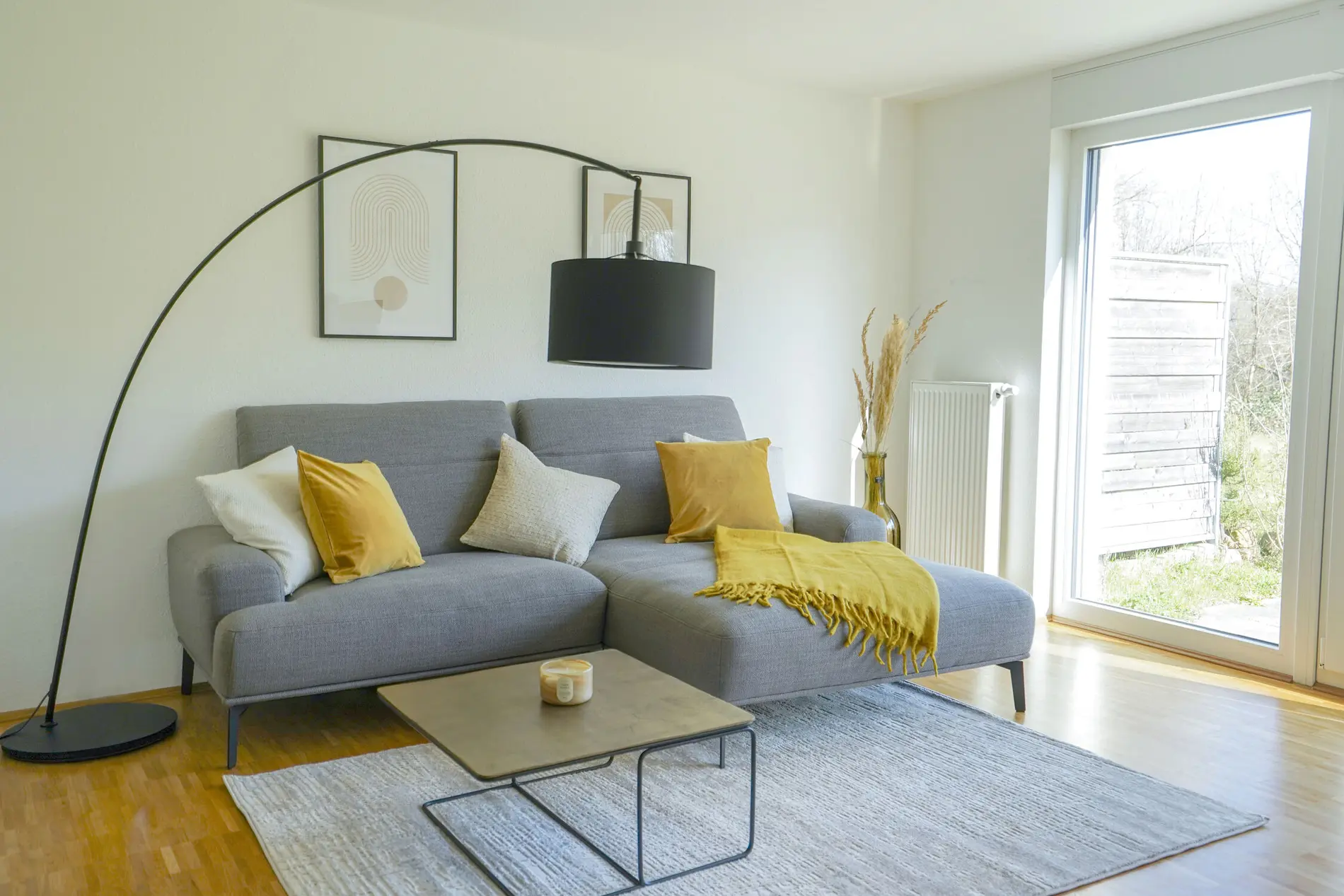 Wohnbereich-weisenburger-Musterhaus Ein großes graues Sofa mit gelben Kissen mit einem Beistelltisch und einer Stehlampe