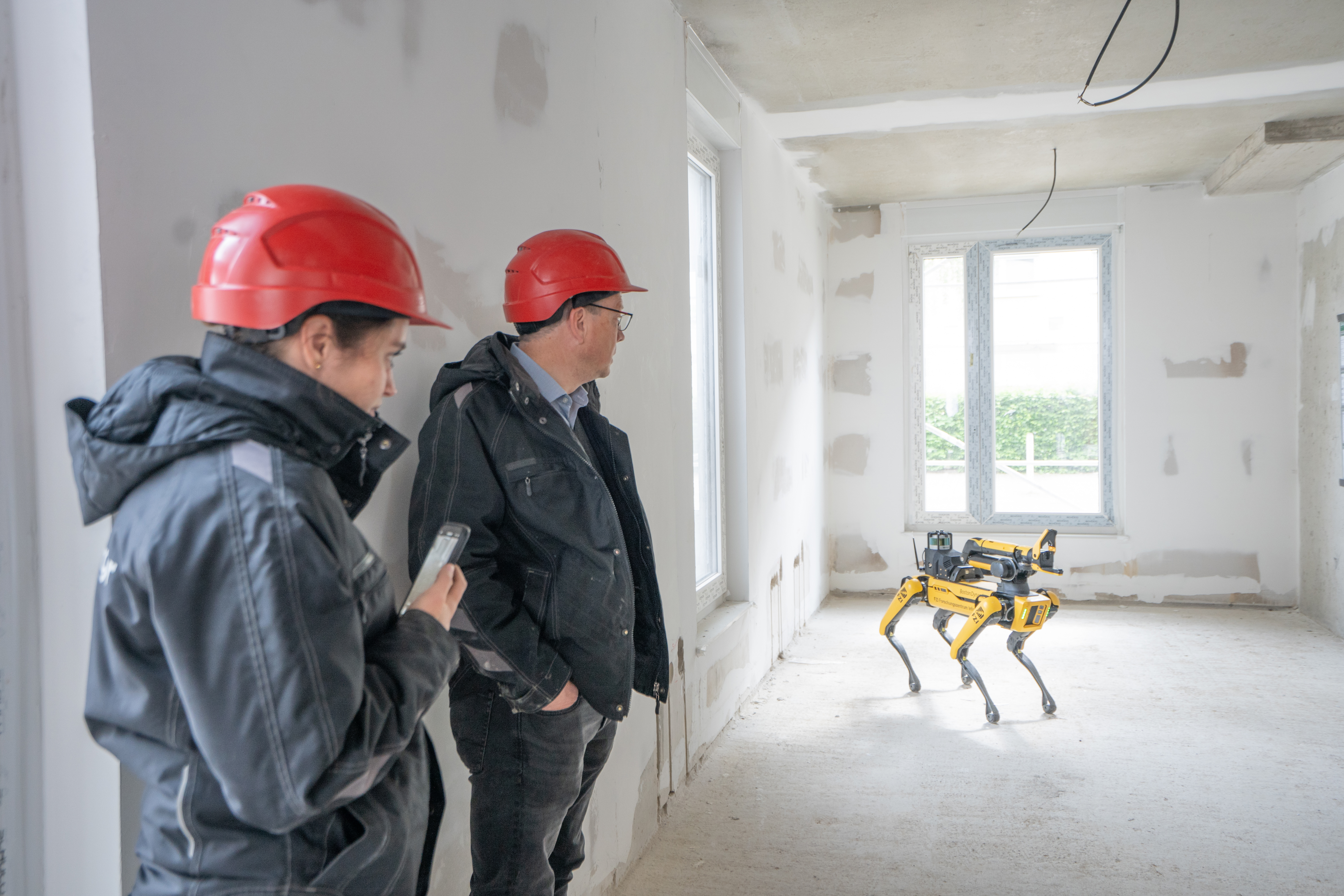 Zwei Männer mit rotem Bauhelm testen einen Robotik auf einer Baustelle